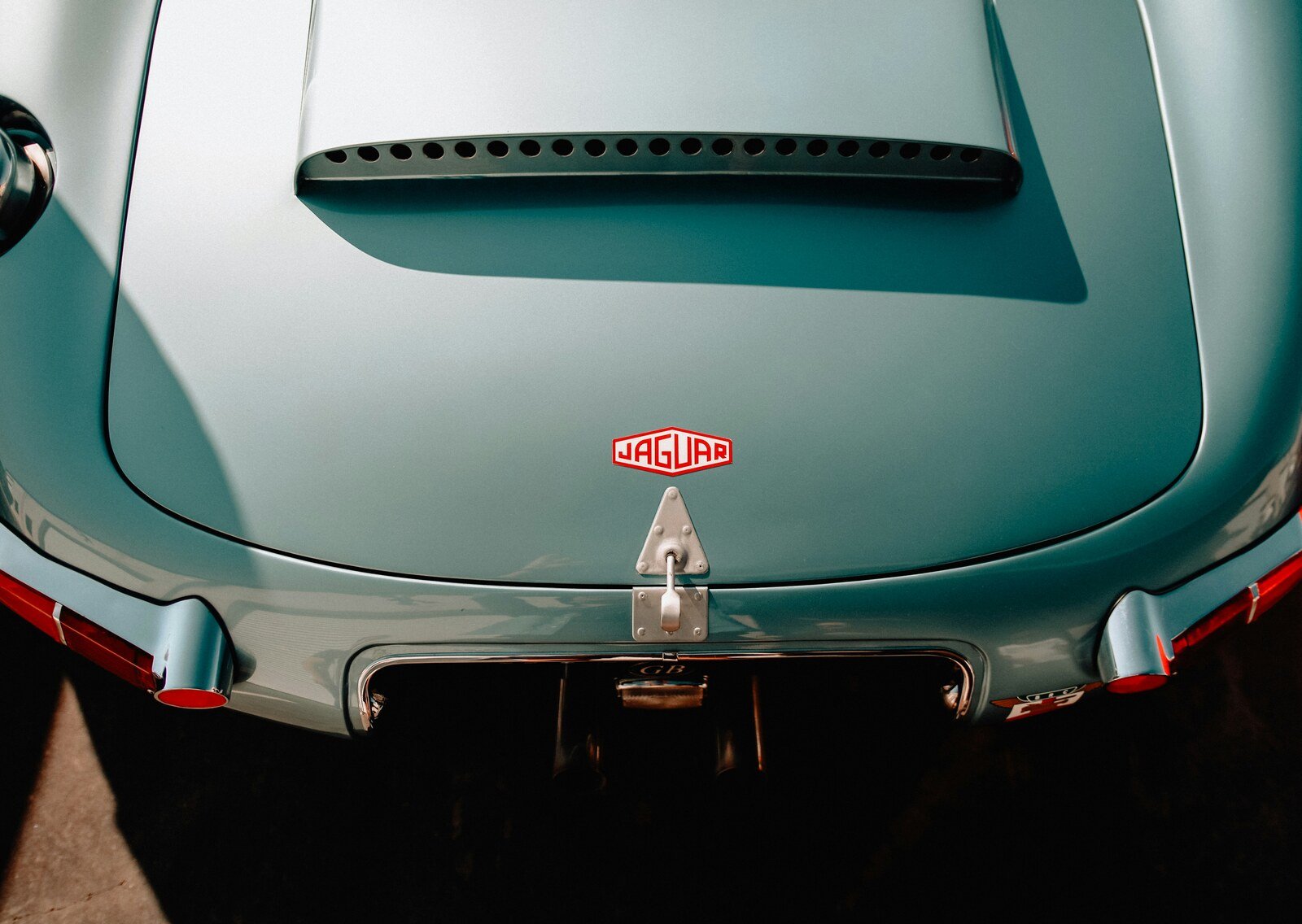 Close-up of the rear of a light blue Jaguar classic car showcasing the vintage Jaguar logo and sleek aerodynamic design