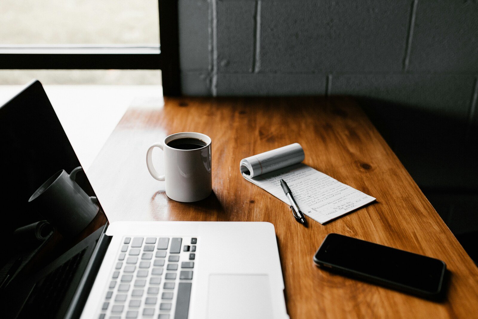 Wooden-desk-with-a-laptop-coffee-mug-notepad-and-pen-showing-a-setup-for-writing-a-blog-to-rank-on-Google