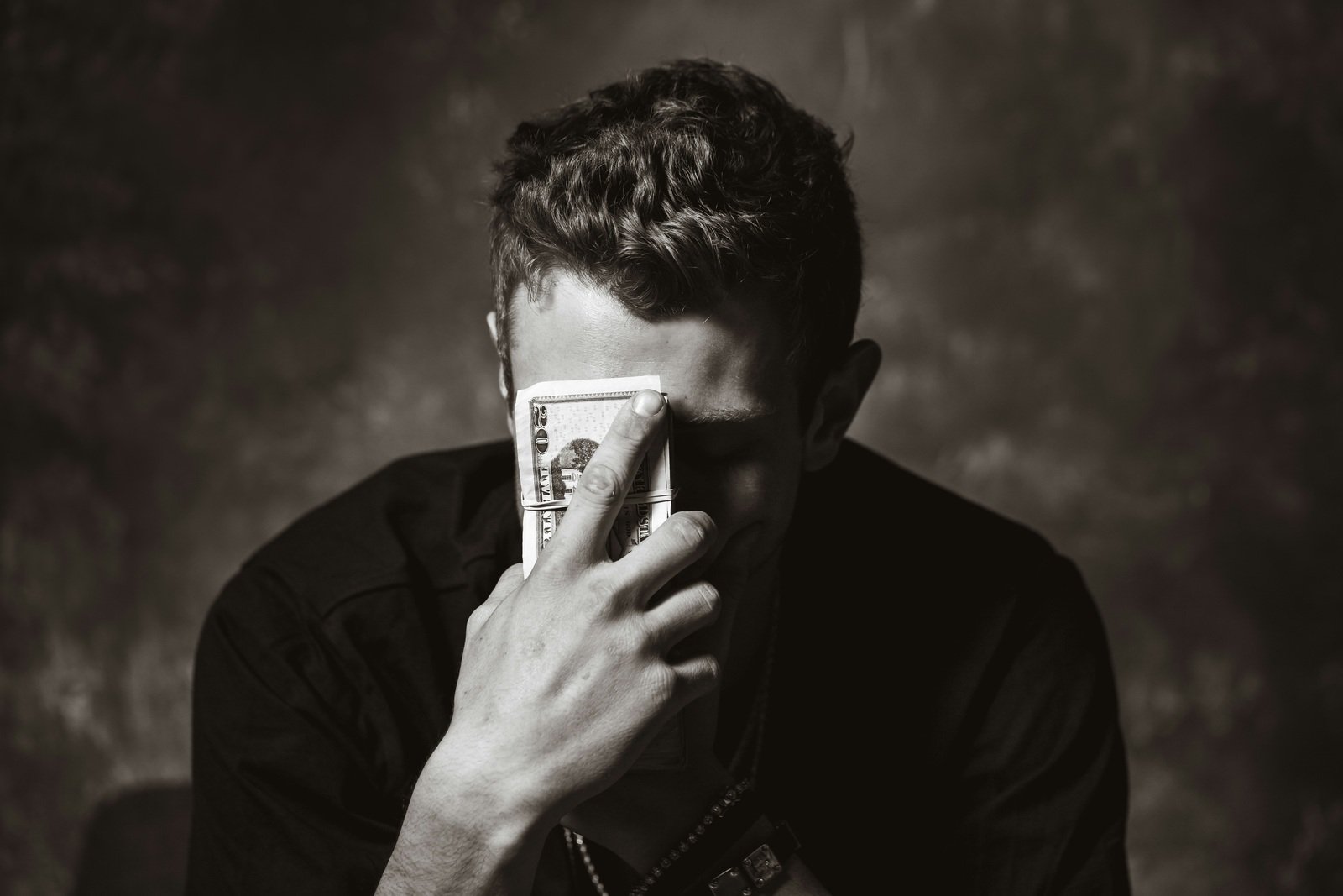 A young man in a black shirt holding a thick stack of hundred-dollar bills against his forehead. Maximize your Google Ads budget and ROI with expert tips from NewFrame Digital