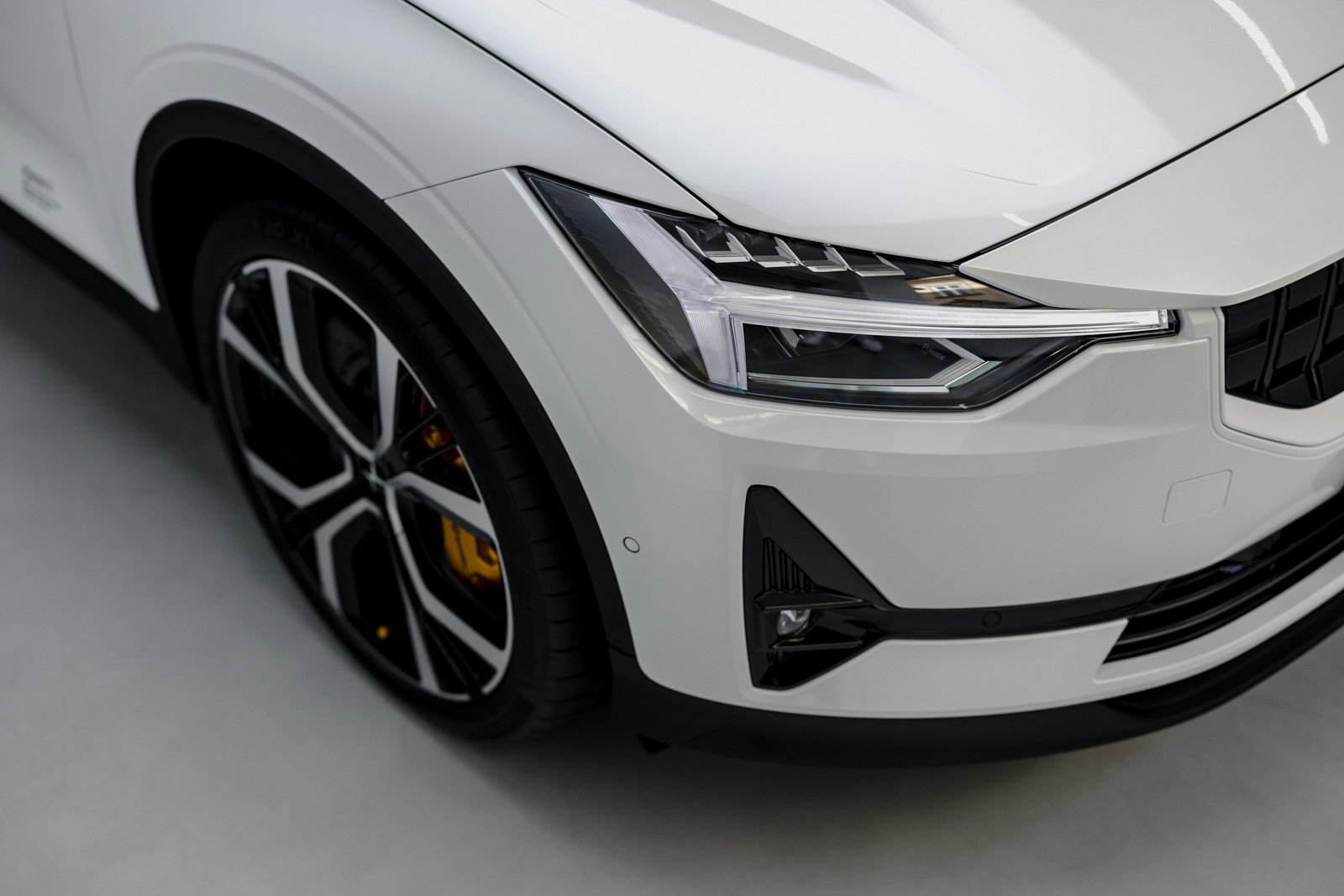 Close-up of a modern white vehicle's sleek headlight and alloy wheel, emphasizing contemporary design and luxury
