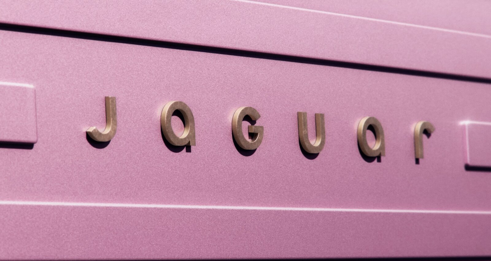 Close-up of Jaguar's rebranded logo in gold lettering on a pink metallic surface, symbolizing elegance and a refreshed identity