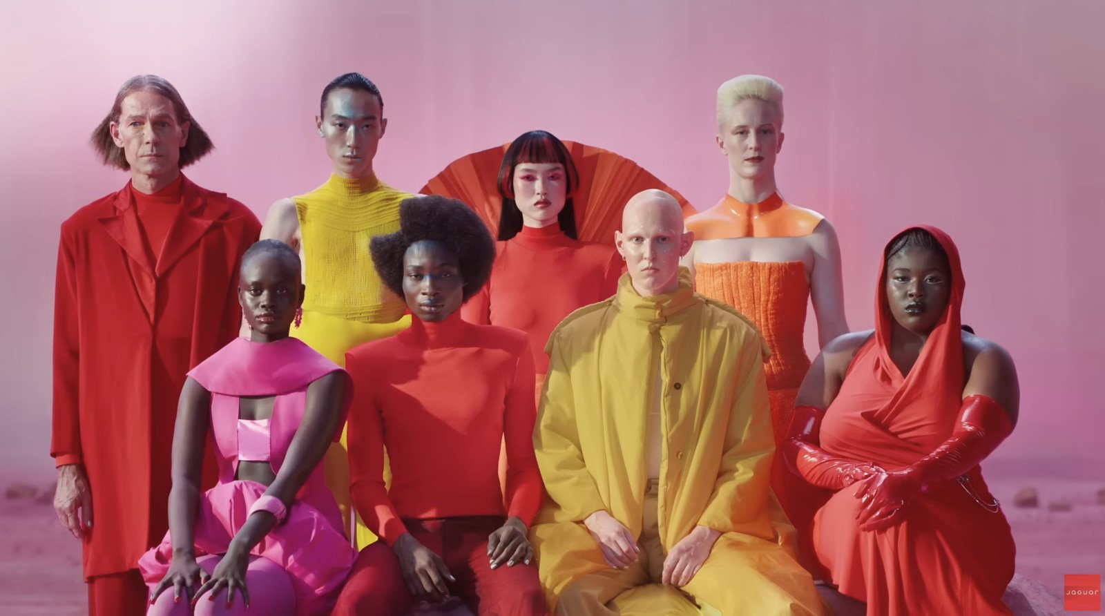 Diverse group of models in vibrant, futuristic outfits, showcasing Jaguar's bold and inclusive rebranding campaign. Pink background emphasizes creativity and modernity.jpg